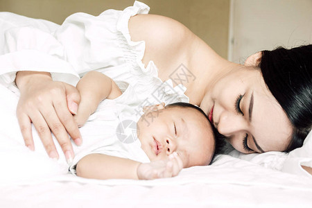 母亲吻和在白床上抱着睡的婴儿手背景图片