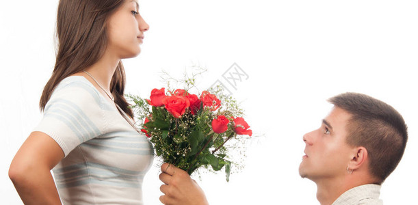 年轻男人跪在地上给他的女朋友送玫瑰花束在白色的图片