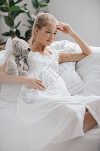 穿着白睡衣和泰迪熊的孕妇肖像在图片