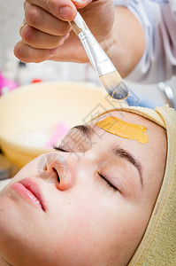 美容师的手在女人脸上涂抹奶油图片