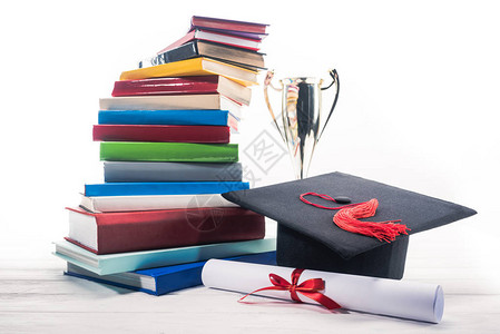 具有文凭和奖杯的毕业帽子由一堆书图片