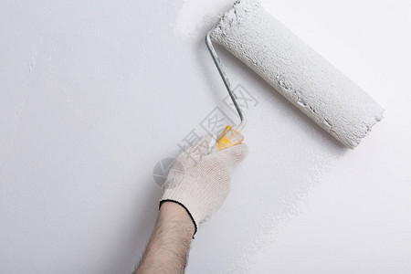 画家手臂用油漆滚筒涂成灰色墙壁的特写图片