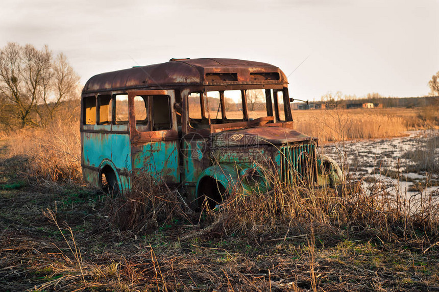 日落时站在田野里的锈迹斑的旧巴士沉闷的风景图片