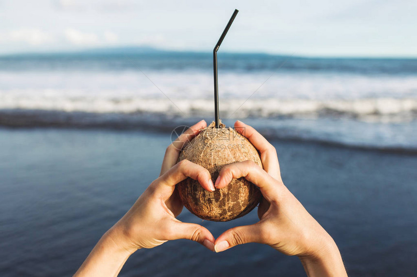 女人的手拿着椰子在巴厘岛的海岸图片