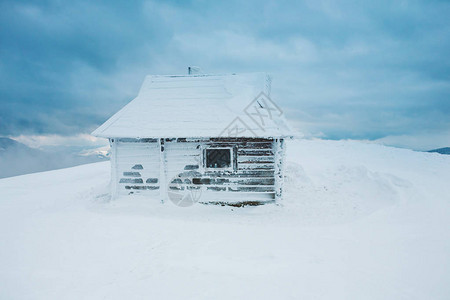 山上的小房子以冬季森林和美丽的云朵天空为背景的白雪覆盖的小图片