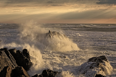 日落时的海景与暴风波冲向悬崖和岩石以太阳光照图片