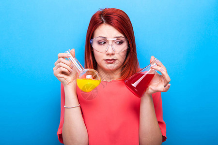 身戴保护眼镜的神经困惑的女科学家携带两管有彩色液体的钢管图片