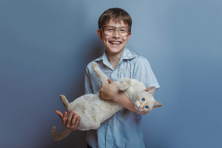 一个10年欧洲外貌的男孩带着眼镜拿着一只猫在灰色背景图片