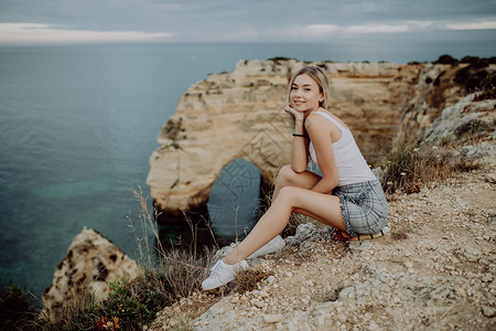 拉丁女孩坐在悬崖上享受葡萄牙大西洋附高清图片