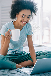 在休息室微笑的非洲女孩穿着咖啡杯和在床上使图片