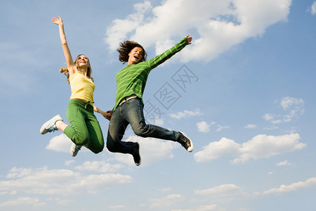 欢快的年轻女孩和男孩跳高与明蓝天空背景图片