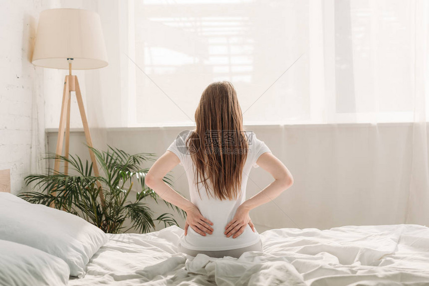 坐在床上和背部疼痛的年轻女图片