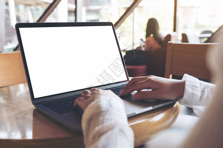在咖啡厅用空白色桌面屏幕在笔记本电脑上使用和打字的商业图片