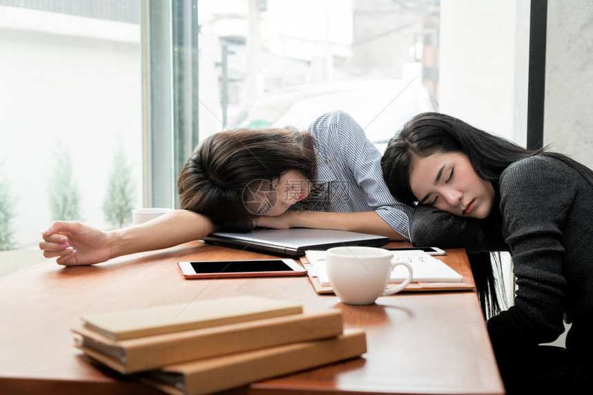 两名亚洲女商人睡在办公室办公桌的笔记本电脑上图片