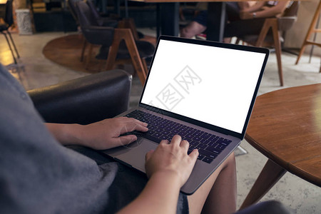 一名妇女坐在椅子上时使用笔记本电脑并用空白桌面屏幕打图片