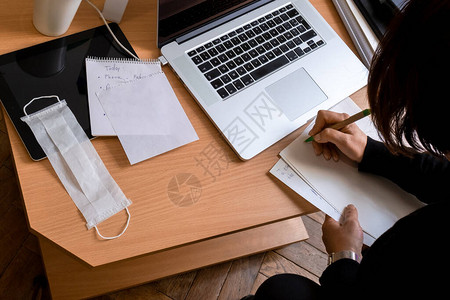 女人在家工作医疗面罩在笔记本电脑上大流行期间工作场所的特写待图片