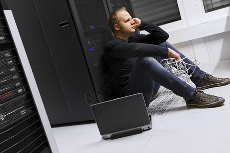 在数据中心的工程师顾问坐在服务器机架前坐着冷酷无情的坐姿背景图片