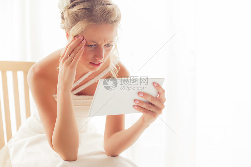 担心的新娘看着坐在窗边的平板电脑图片