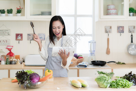 快乐的亚洲年轻女子正在厨房里高兴地做饭图片