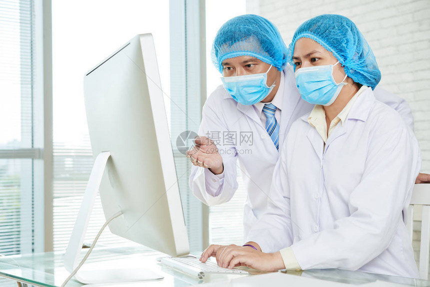 戴着医用口罩和白大褂的医生在实验室的电脑显示器上图片