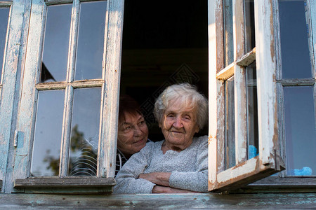 老年妇女和成年女儿向村舍窗外看望图片