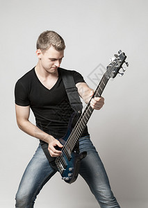 年轻男音乐家演奏六弦贝斯吉他在光背景图片