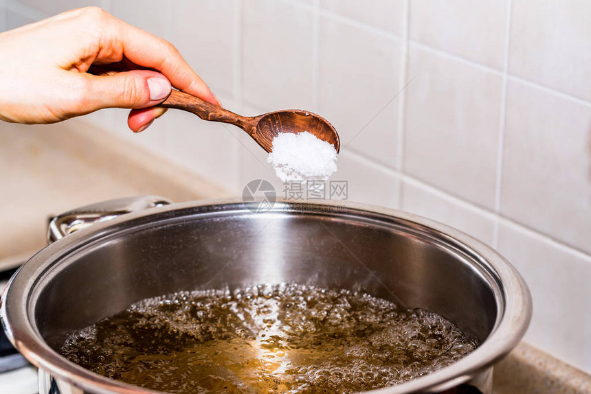 用木勺关闭手在平底锅的沸水中加盐准备汤图片