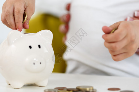 孩子的手把零钱硬币放入白色的存钱罐槽中预算费用概念使储蓄和有效的投资理念背景图片