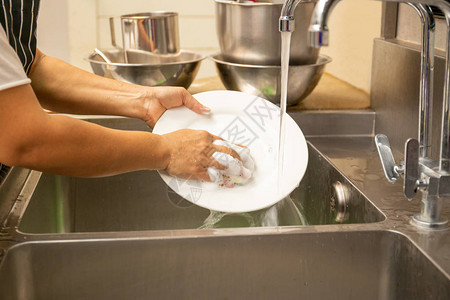手在水槽里用自来水洗脏盘子背景图片