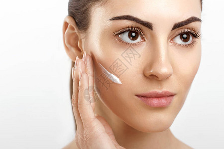 美丽的年轻女子与清洁新鲜皮肤应用奶油和触摸自己的脸部护理美容图片