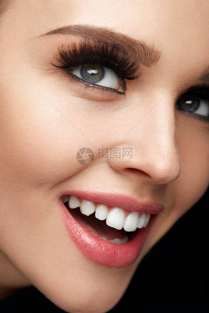 美容化妆美丽微笑的女人脸与长而浓密的假睫毛和完美的面部化妆的特写快乐感的女图片