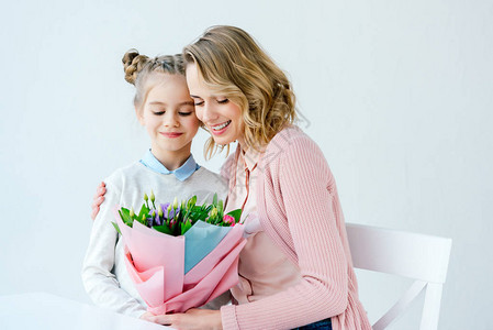 微笑的母亲用美丽的花束拥抱小女儿的肖像图片