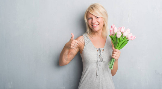 白人成年女在灰色的格朗基墙上拿着粉红色的花图片