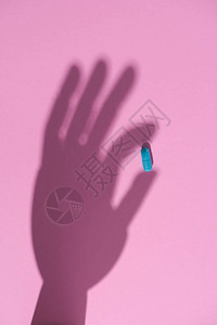 粉红色表面握着蓝色药丸的手背景图片