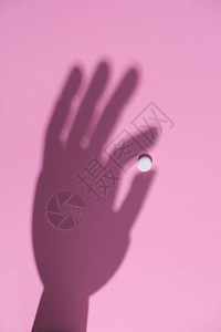 粉红色表面握有白药片的手背景图片