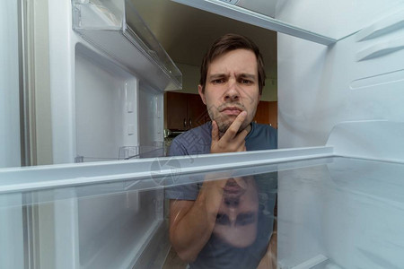 饥饿的人正在空冰箱里找食物图片