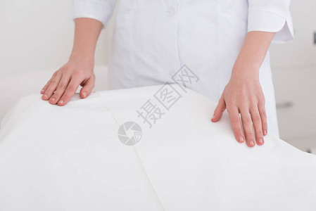 美容师在沙发上站在空按摩桌旁的白色大衣上的图片