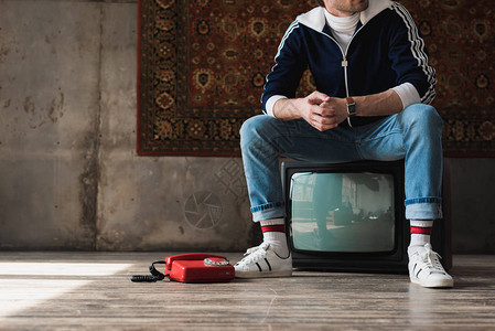 穿着古老衣服的英俊年轻男子坐在旧式电视机上图片