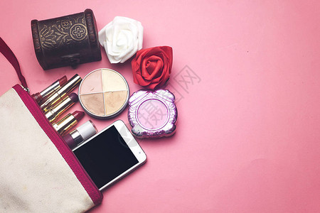 化妆包里有不同颜色的口红粉饼和手机粉色背景上红色和白色图片