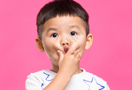 亚洲小男孩用手抚摸粉红色背景的脸颊图片