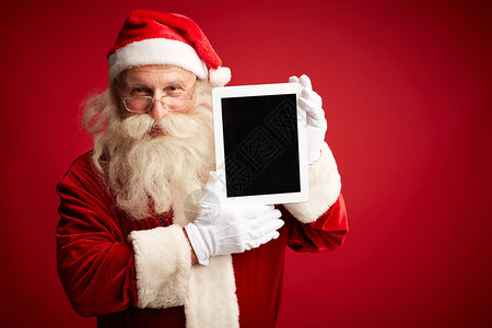 圣诞老人拿着触摸板看着红背景图片
