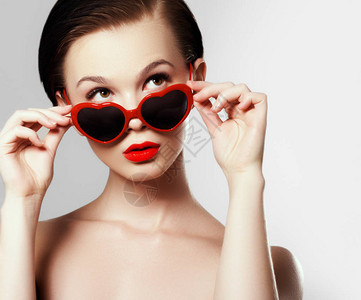 戴眼镜的年轻女孩以心的形式节日化妆美丽感的嘴唇情人节的概念图片
