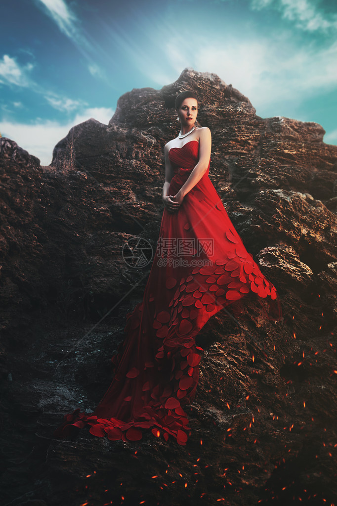 穿着长红裙子的年轻美女站在岩石图片