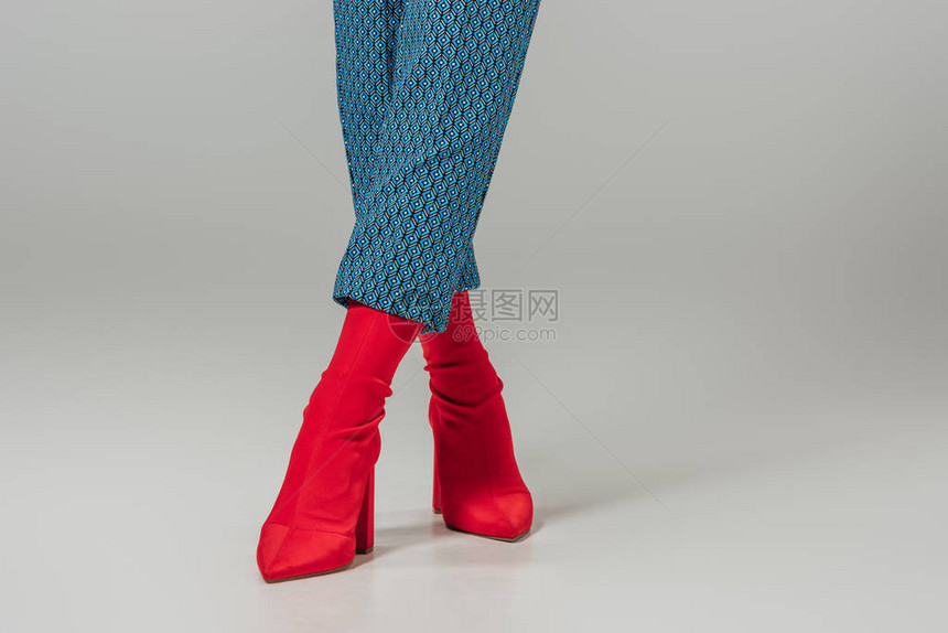 灰色背景下穿着红色时尚靴子的女腿的裁剪图像图片