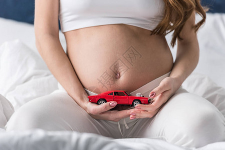 孕妇拿着红色玩具车的剪影图片