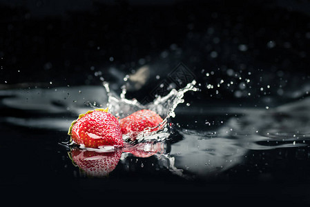 熟的草莓掉入水中在黑图片