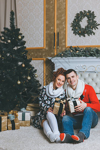 快乐的一对年轻夫妇拿着两个礼物盒在壁炉附近庆祝圣诞节快乐的2017图片