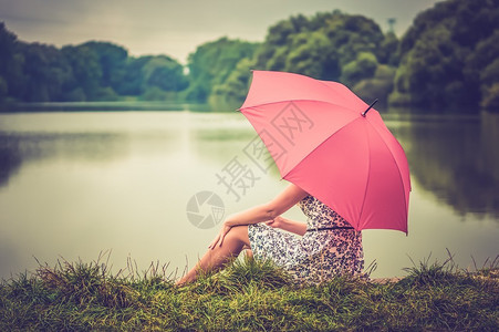 年轻美丽的女士在池塘附近坐着红色雨伞外望遥远的处复图片