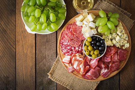 木制背景上配有培根肉干意大利腊肠奶酪和葡萄的开胃菜餐饮背景图片