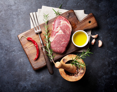 生牛排烹饪和配料肉片香草和香料石桌上的顶视图图片